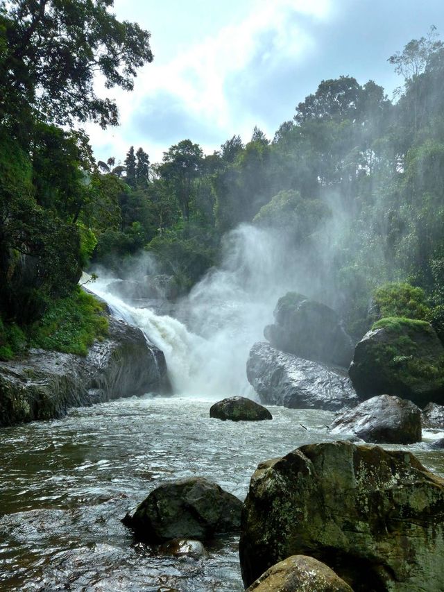 A waterfall throws spray over large boulders in a green forest